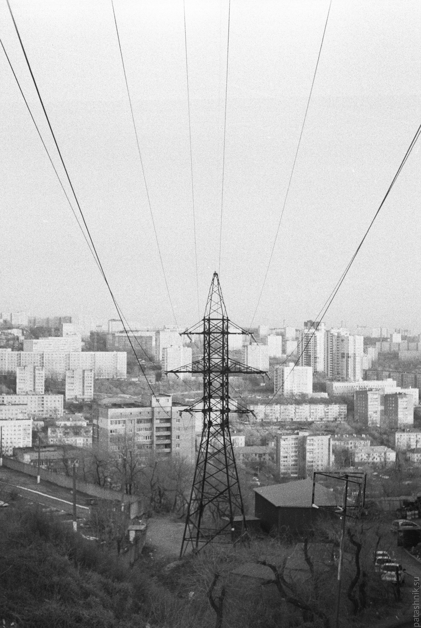 Transmission tower, power liens running downhill and buildings on background